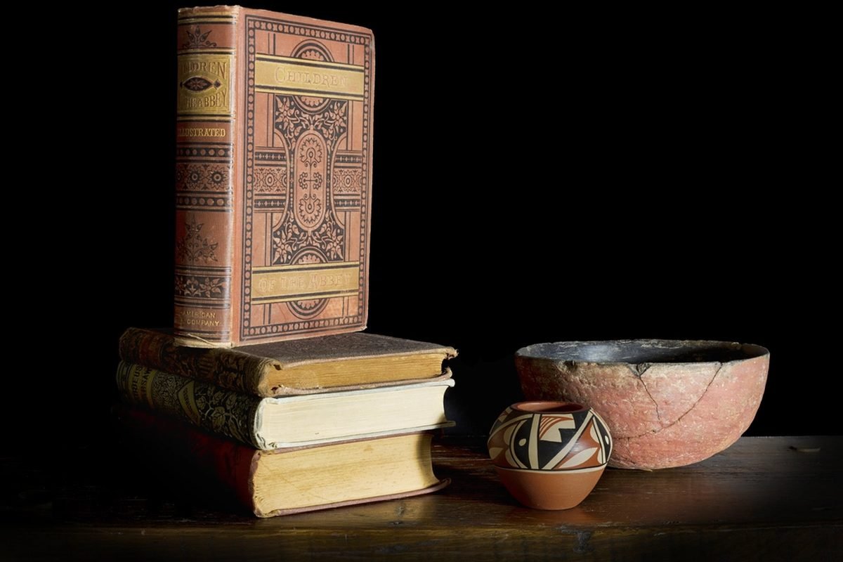 A stack of old hardbound books beside a clay bowl.