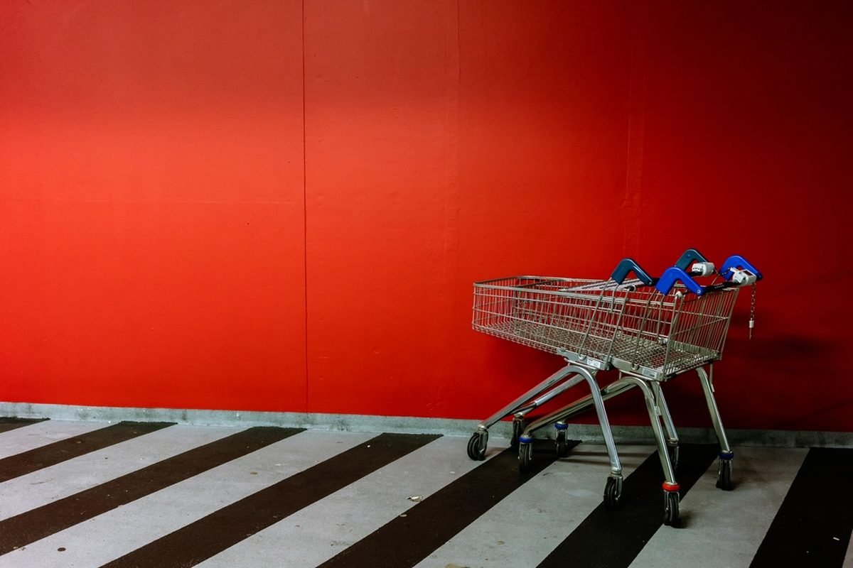 A supermarket trolley against a plain red wall.