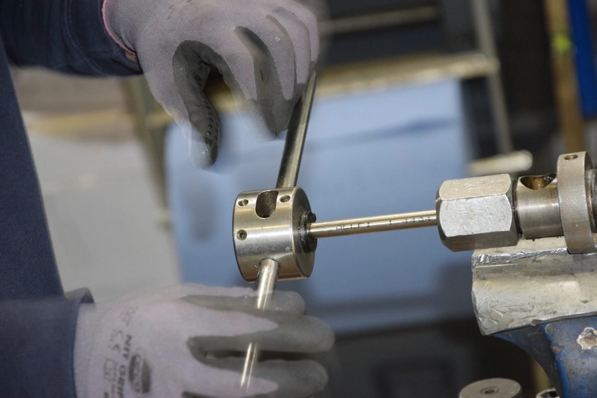 Gloved hands working a metal part on a lathe.